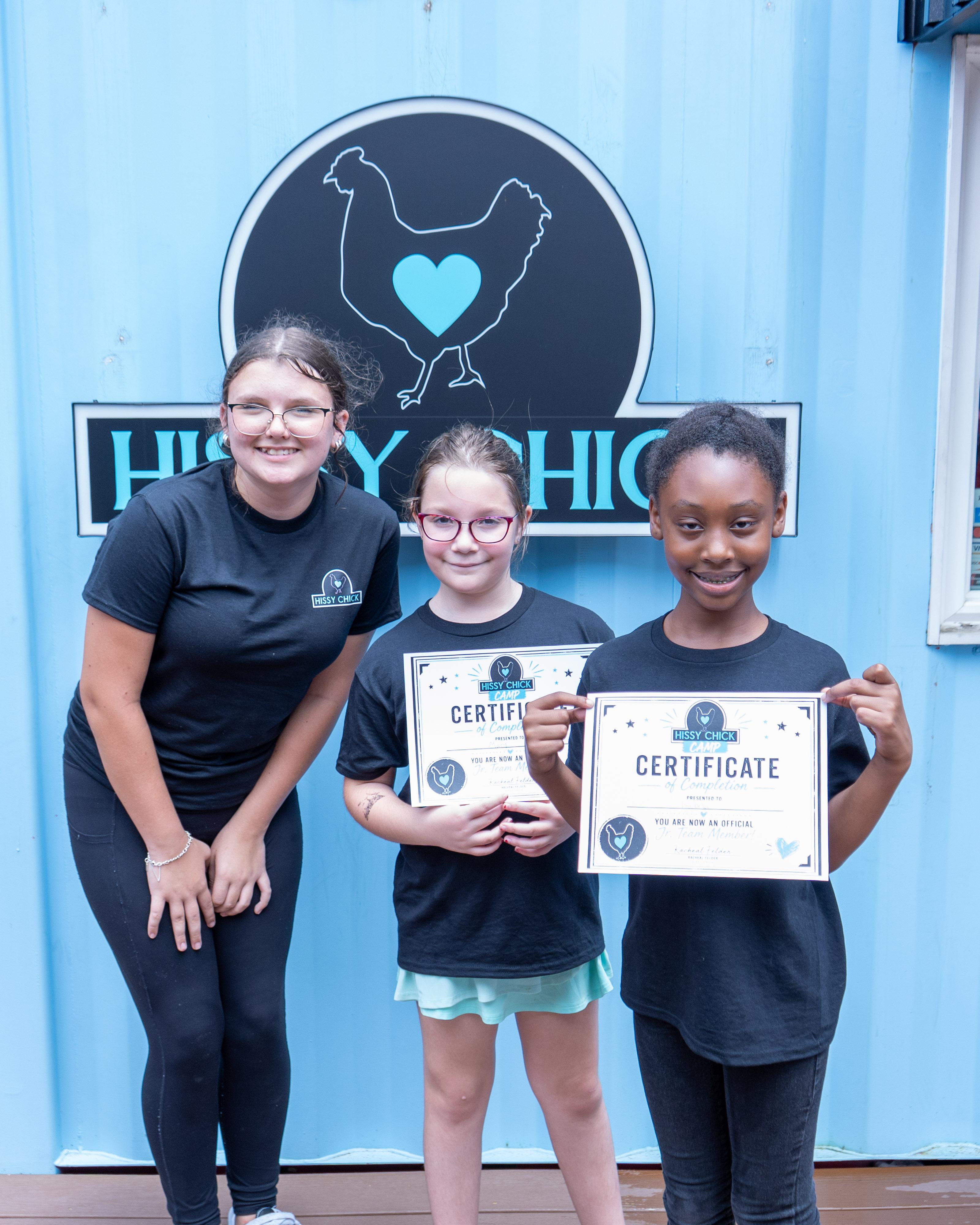 Hissy Chick campers holding completion certificates in front of the storefront